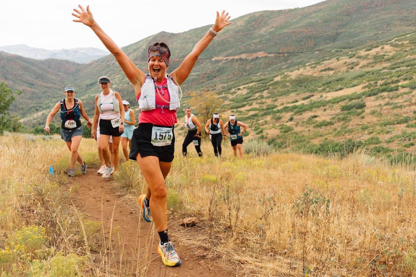 A runner coming up the trail with both arms thrown wide.