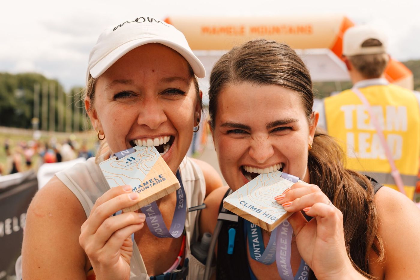 Two runners grinning and biting their finisher medals at the finish arch.
