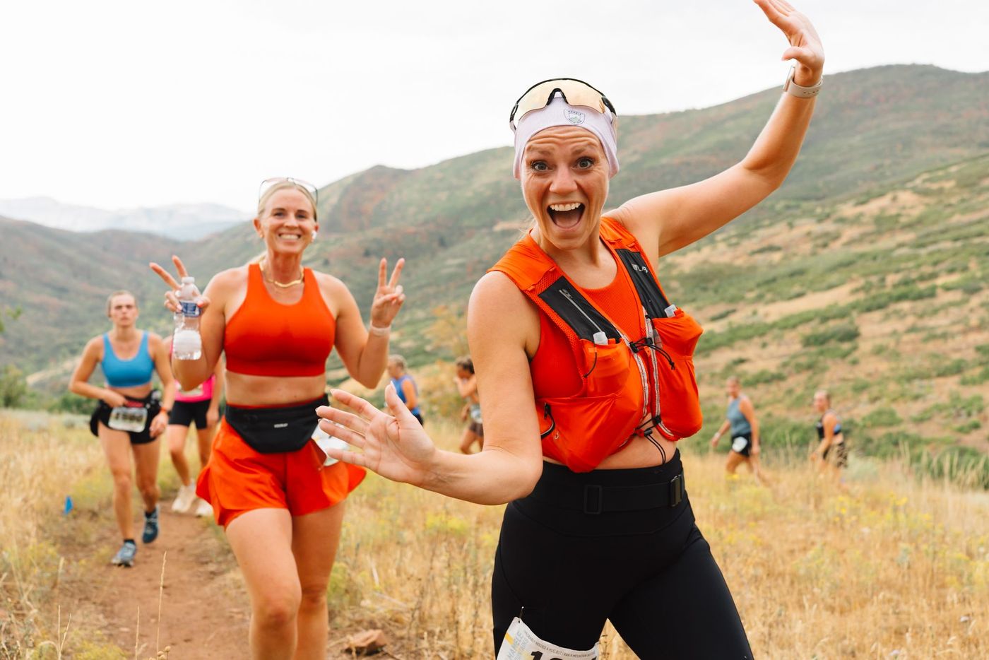 Two runners waving on the trail.